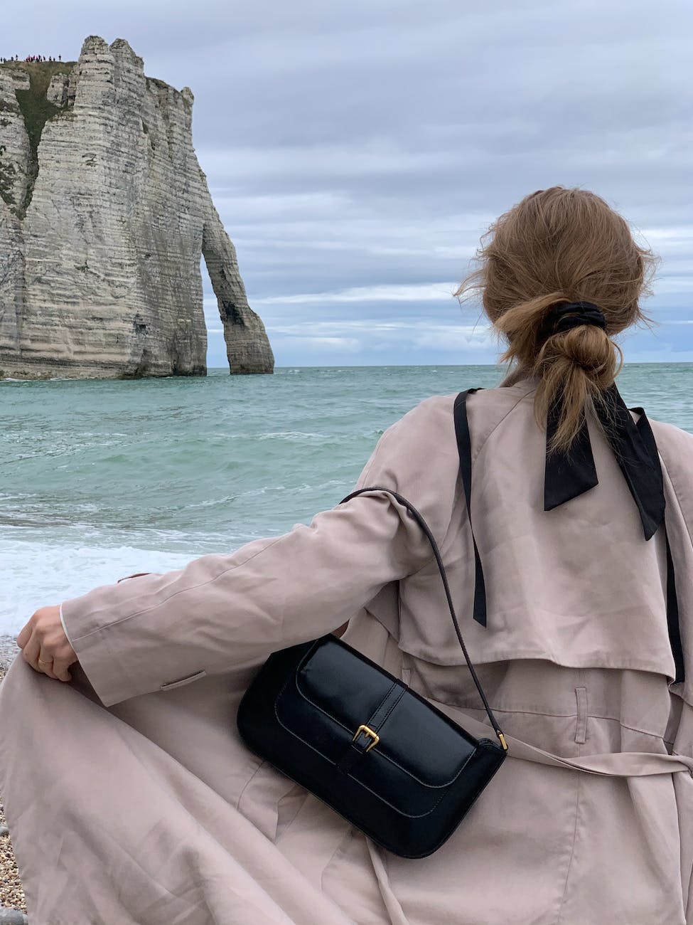 a person in a trench coat standing near the falaise d aval