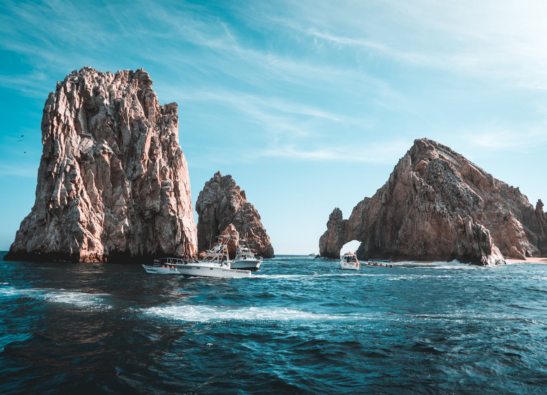 photo of boats on ocean near rock formations